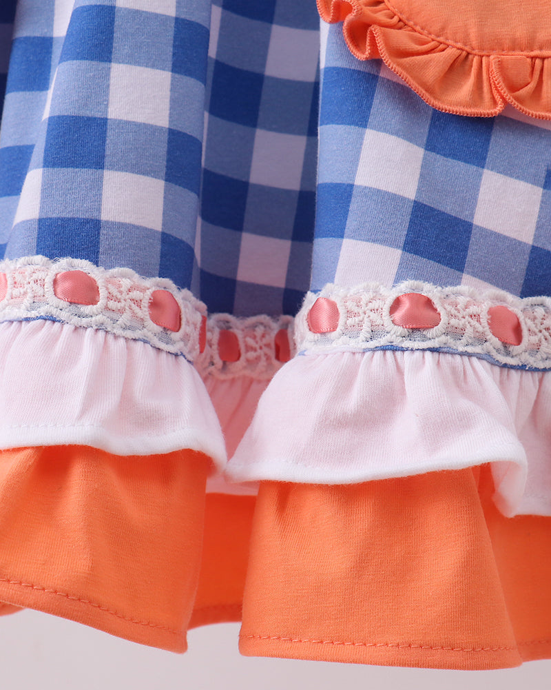 Close-up of a dress with blue checkered, orange, and white ruffled layers on a light gray background.