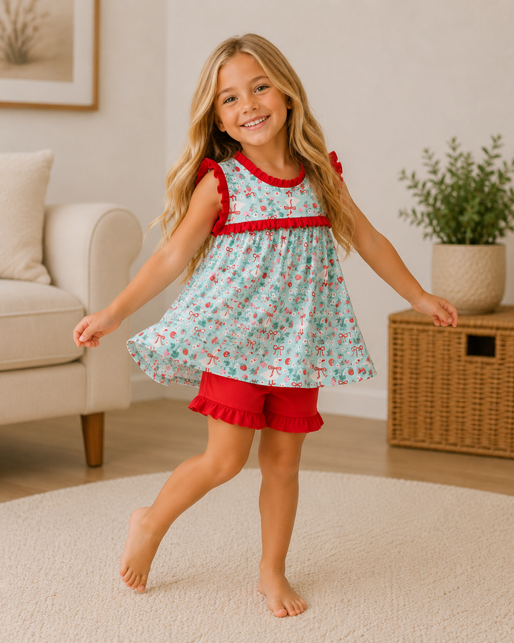 Young girl in a floral dress with red trim and shorts standing in a living room.