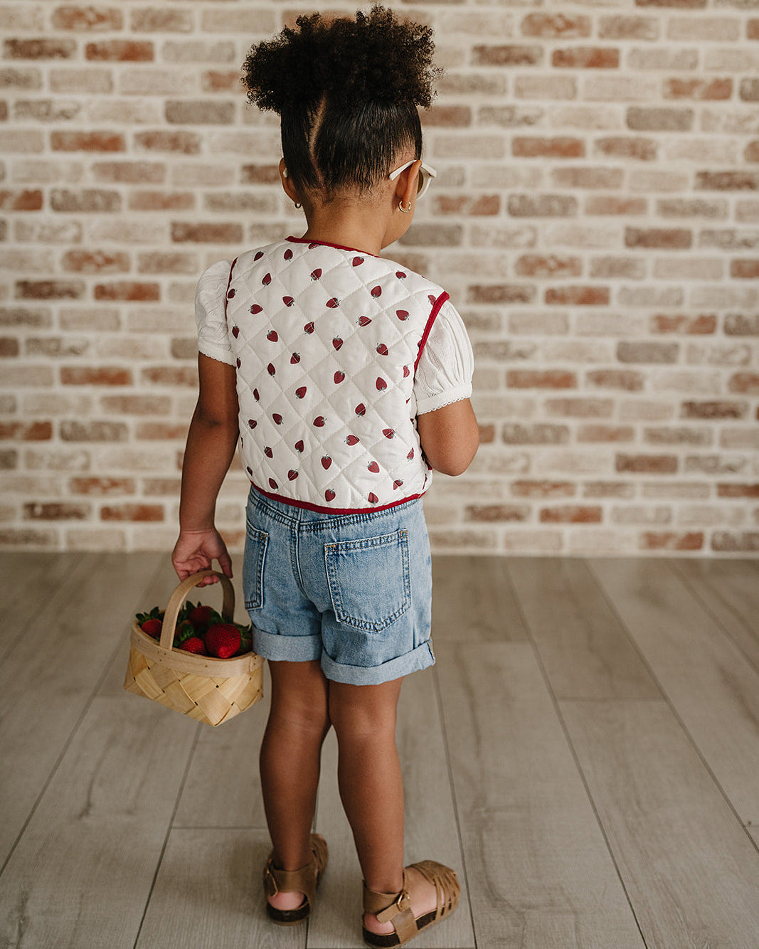 Child holding a basket with berries against a brick wall.