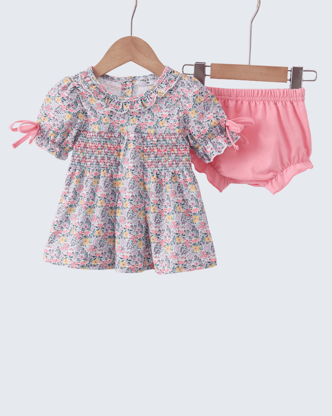 Children's floral top and pink bloomers on hangers against a white background