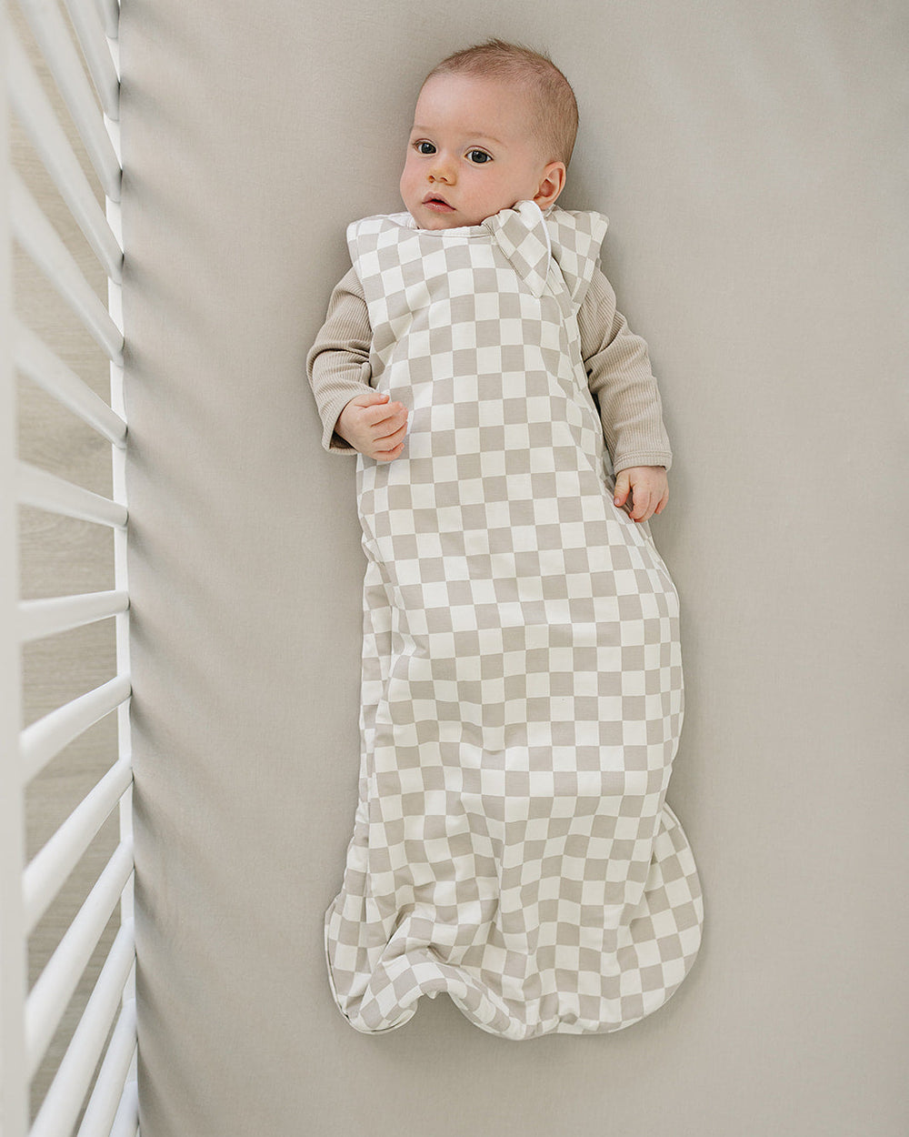 Baby wrapped in a checkered sleep sack lying on a neutral-colored surface.