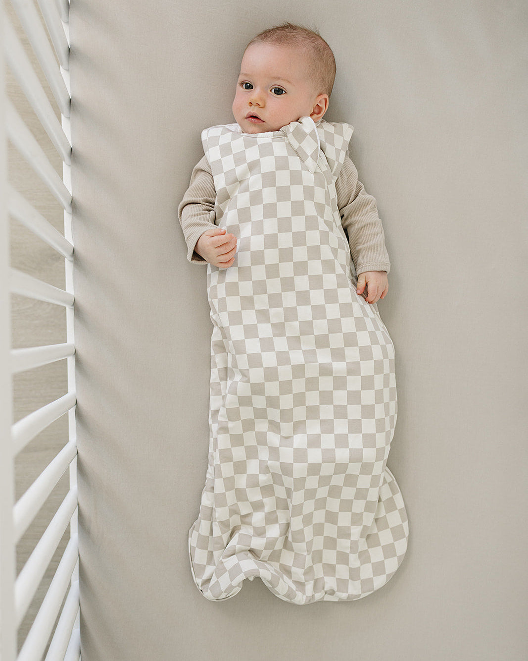 Baby wrapped in a checkered sleep sack lying on a neutral-colored surface.