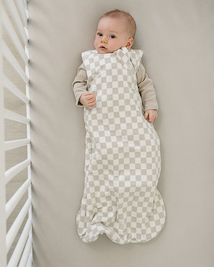 Baby wrapped in a checkered sleep sack lying on a neutral-colored surface.