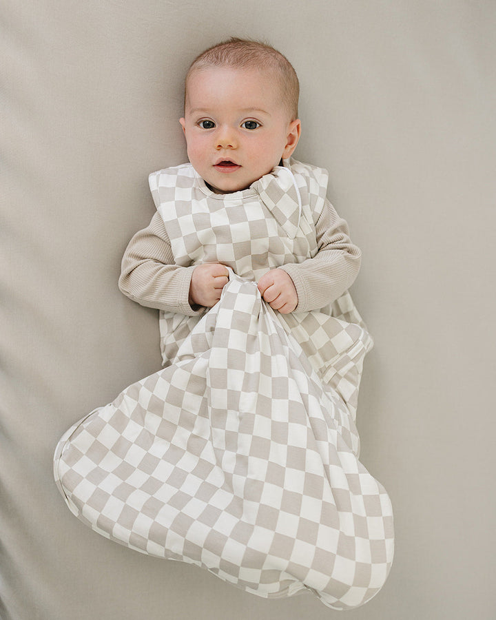 Baby wrapped in a checkered sleep sack on a neutral background