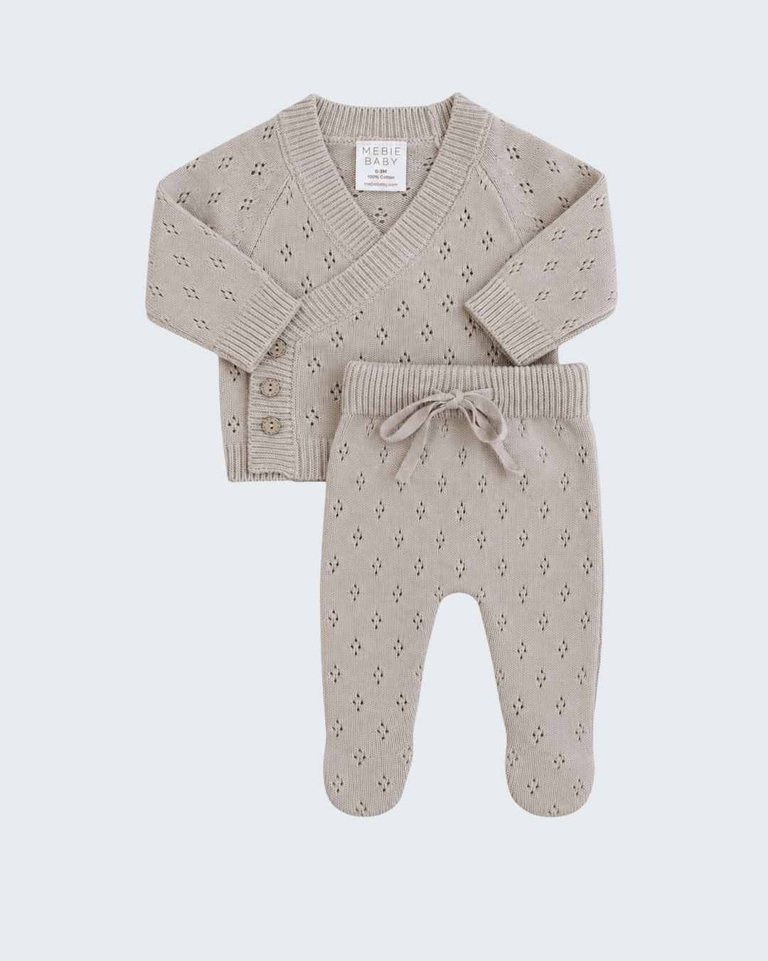 A baby knit two-piece outfit set in a light oatmeal beige color, featuring a long-sleeve V-neck cardigan with button details and matching footed pants with a drawstring waist, laid flat against a light gray background.