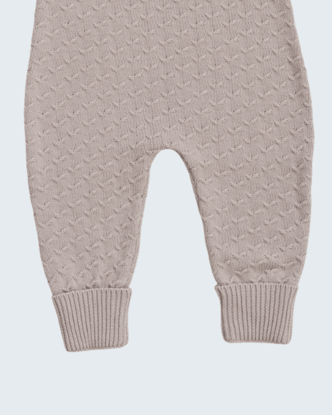 Close-up of a baby knit romper or jumpsuit in a light taupe-beige color, showing the textured knit pattern and ribbed ankle cuffs on a light gray background.