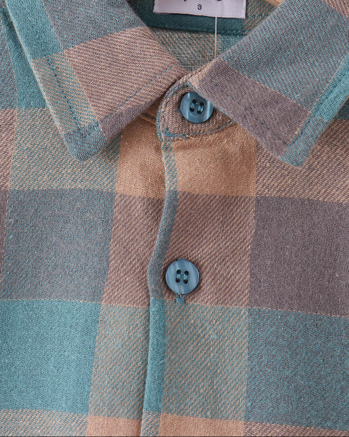 A close-up of a plaid button-up shirt on a wooden hanger, featuring a muted teal, taupe, and beige check pattern with matching blue buttons. The neck label reads &