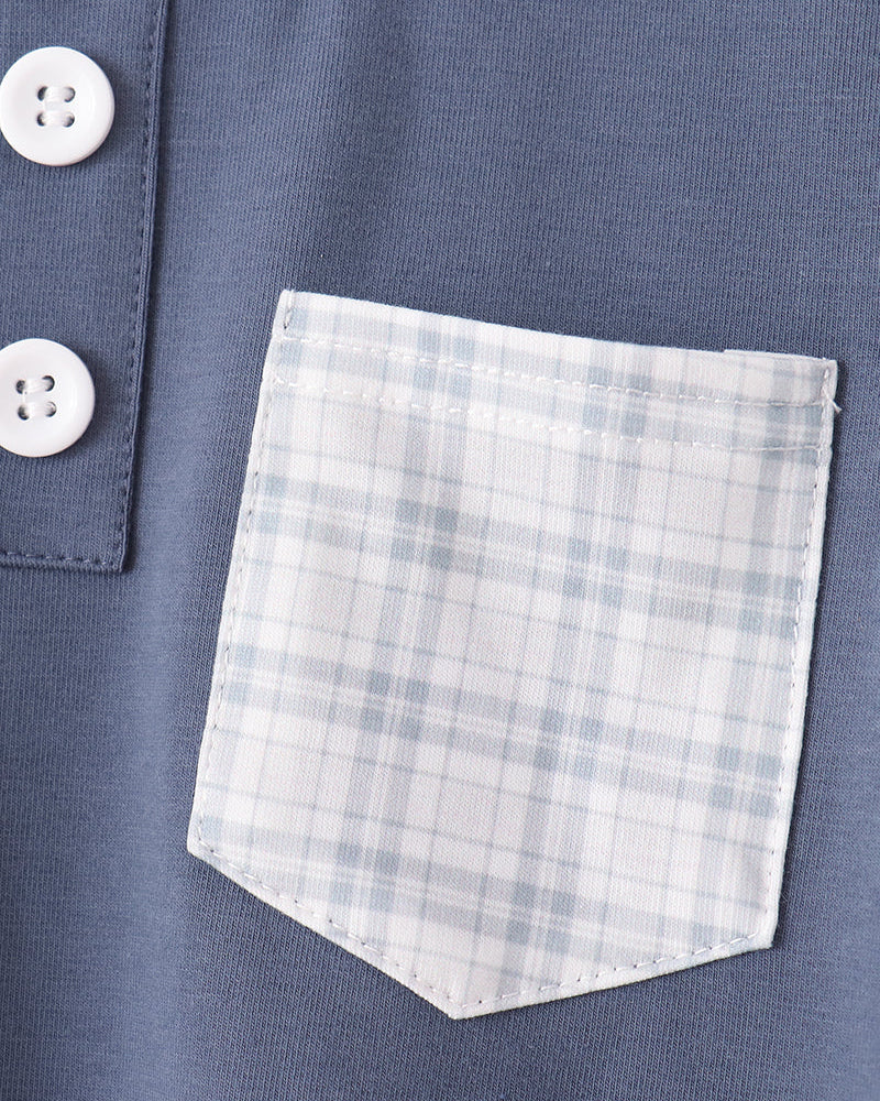 Close-up of a blue knit top with a white and light blue plaid chest pocket and two white buttons on the left side.
