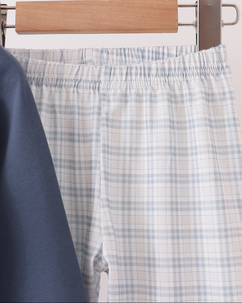 Light blue and white plaid  pants hanging on a wooden hanger, with a dark navy garment partially visible in the foreground.