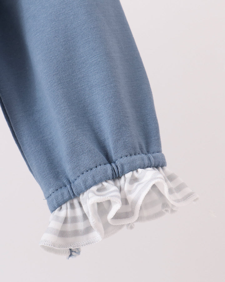Close-up of a light blue knit garment, likely a baby jacket or pants leg, with a gathered cuff and a ruffled white striped trim.