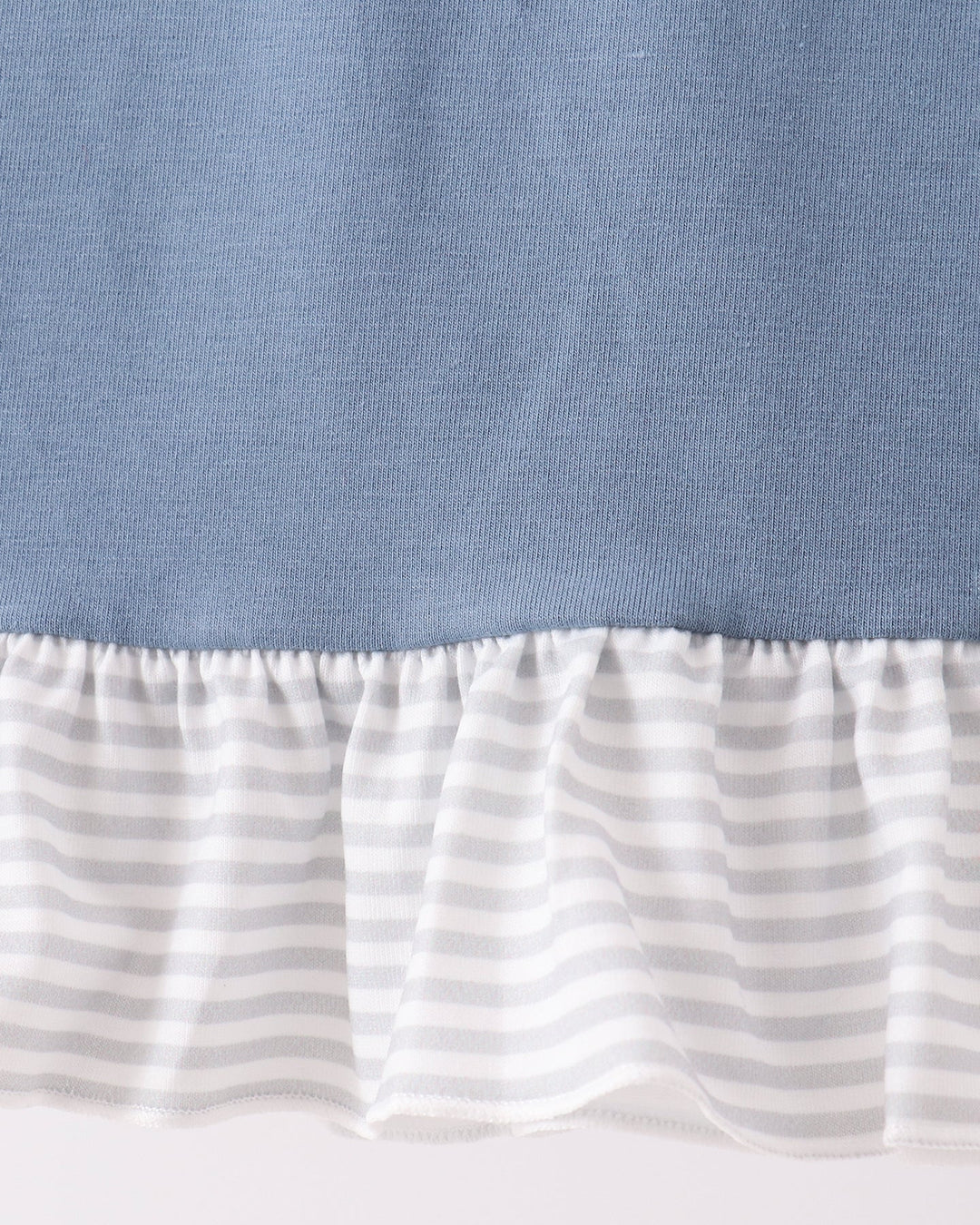 Close-up of a ruffled hem detail showing a solid dusty blue upper section and a white ruffle with thin gray horizontal stripes below.