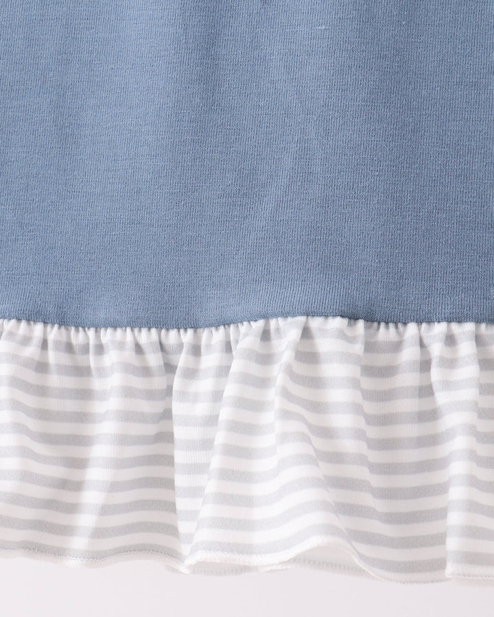 Close-up of a ruffled hem detail showing a solid dusty blue upper section and a white ruffle with thin gray horizontal stripes below.