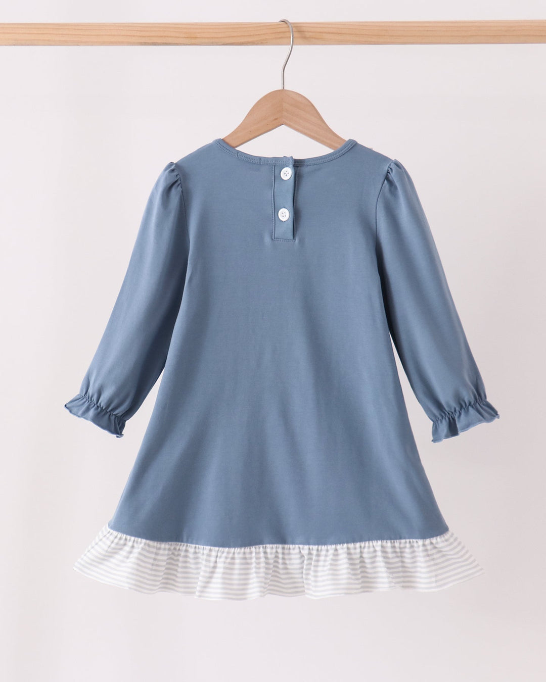 A dusty blue long-sleeve dress for toddlers, shown from the back on a wooden hanger. The dress features a three-button neckline, gathered cuffs, and a white and gray striped ruffled hem.