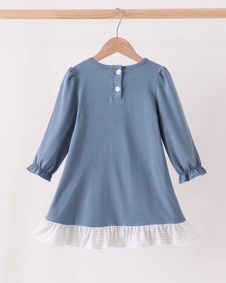 A dusty blue long-sleeve dress for toddlers, shown from the back on a wooden hanger. The dress features a three-button neckline, gathered cuffs, and a white and gray striped ruffled hem.