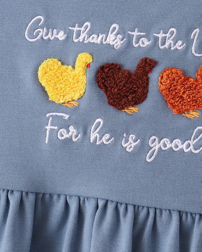 Close-up of a dusty blue baby dress featuring white embroidered text that reads &