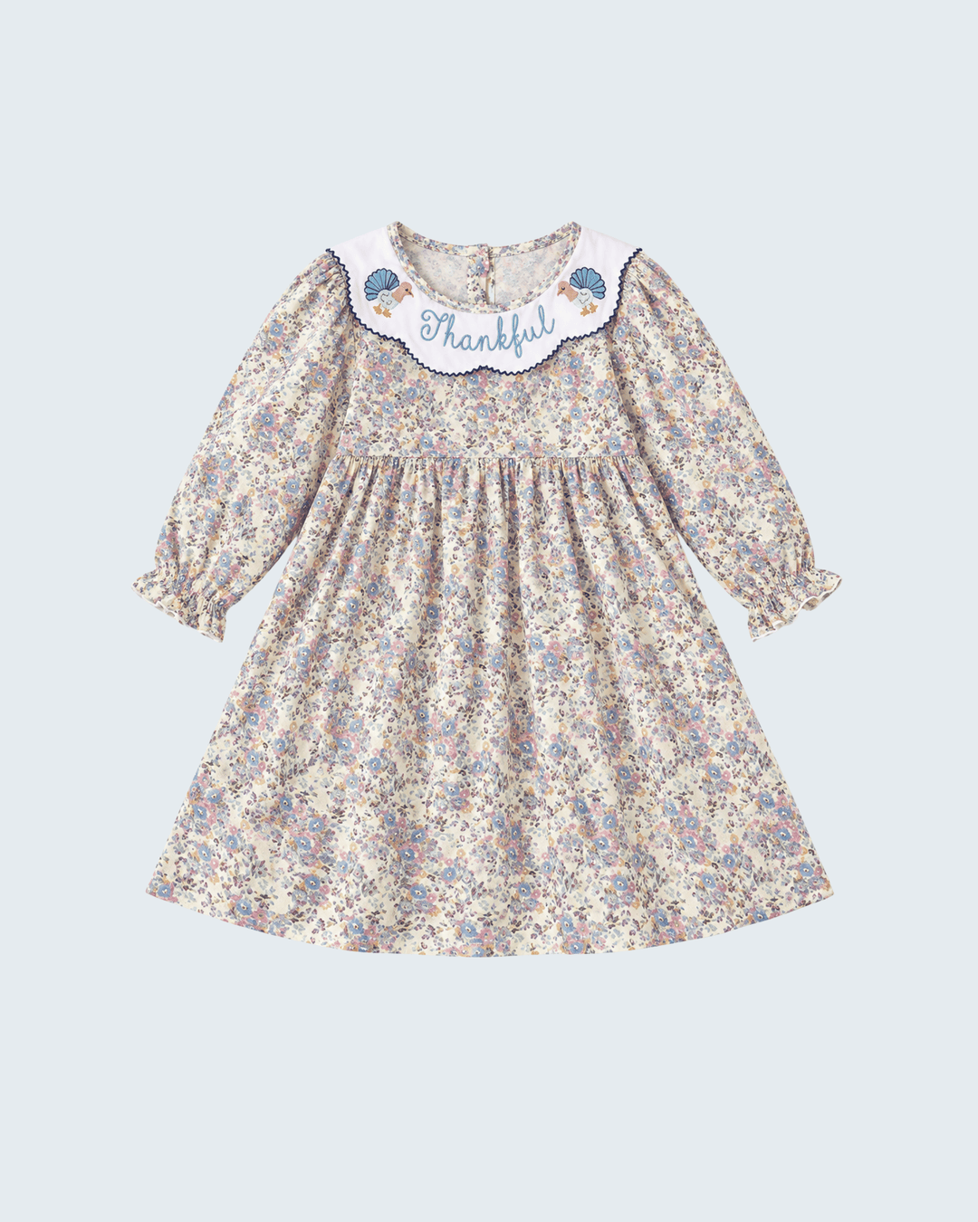A toddler girl's long-sleeve dress with a beige, blue, and purple floral print. It features a white Peter Pan collar decorated with blue birds and the word 'Thankful' embroidered in blue script.