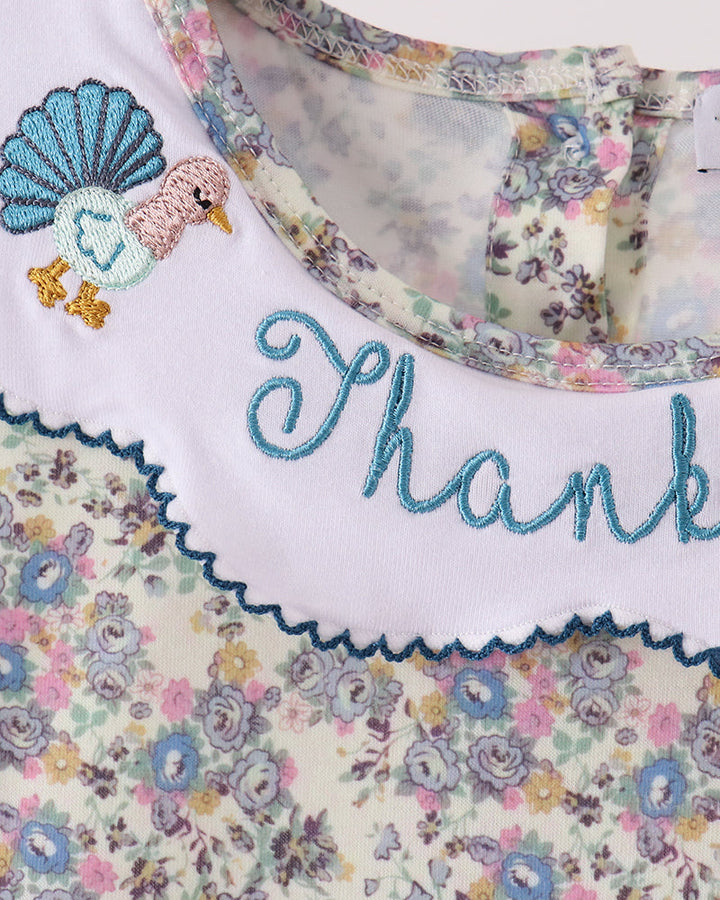 Close-up of a baby top featuring a white collar with blue embroidered script reading &