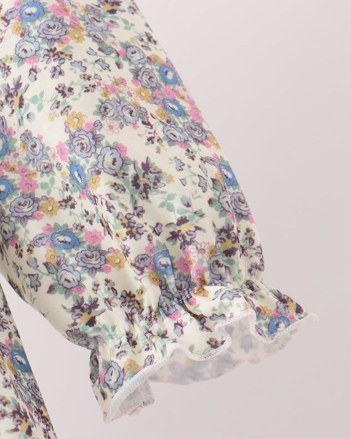 A close-up of a floral-patterned fabric sleeve with ruffled trim, featuring a delicate print of blue, pink, yellow, and purple flowers on a cream background.