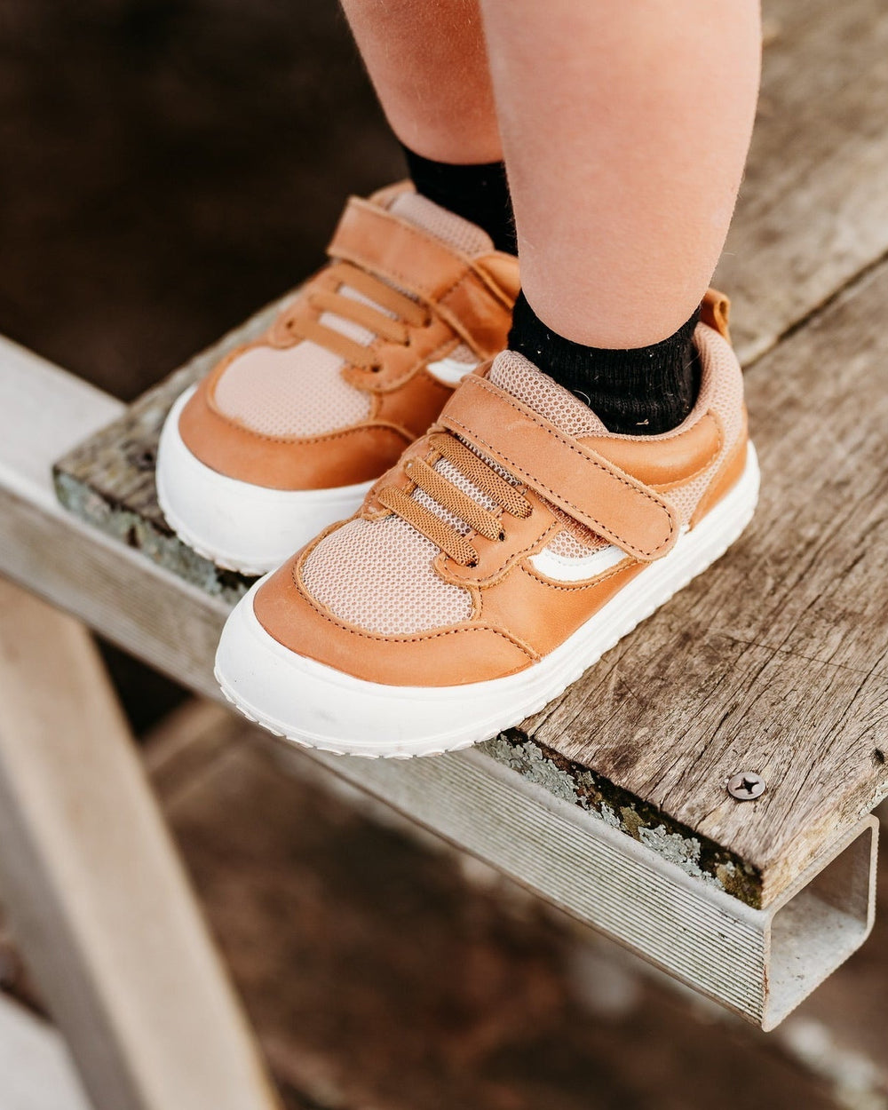 Close-up of tan kids sneakers with hook-and-loop straps on wooden step