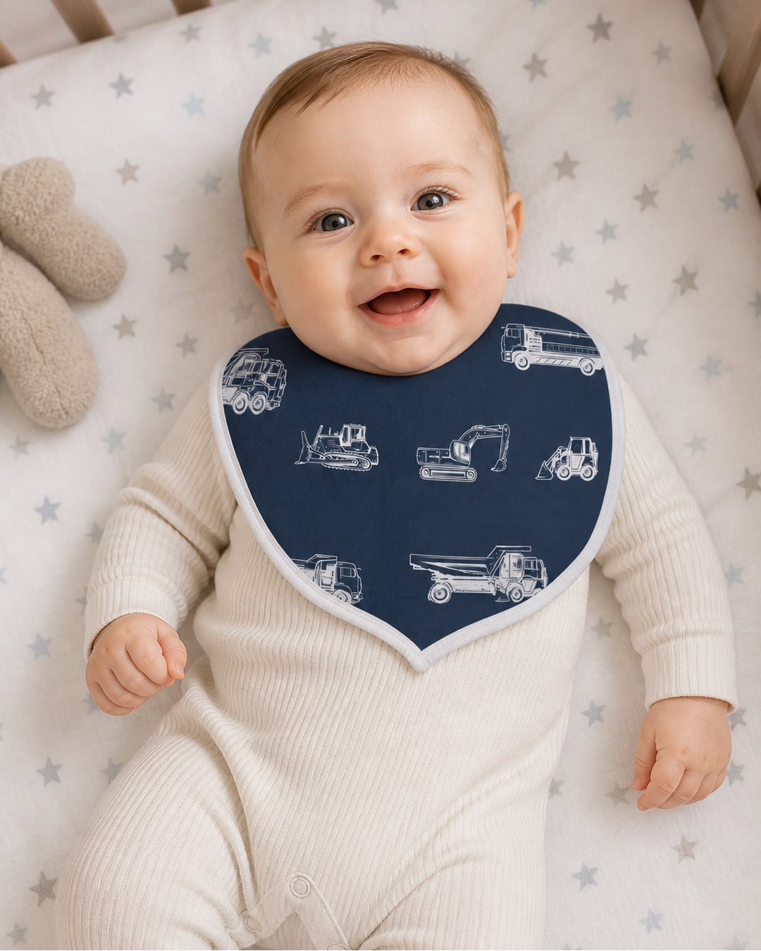 Baby wearing a navy blue bib with white vehicle patterns on a star-patterned crib sheet.