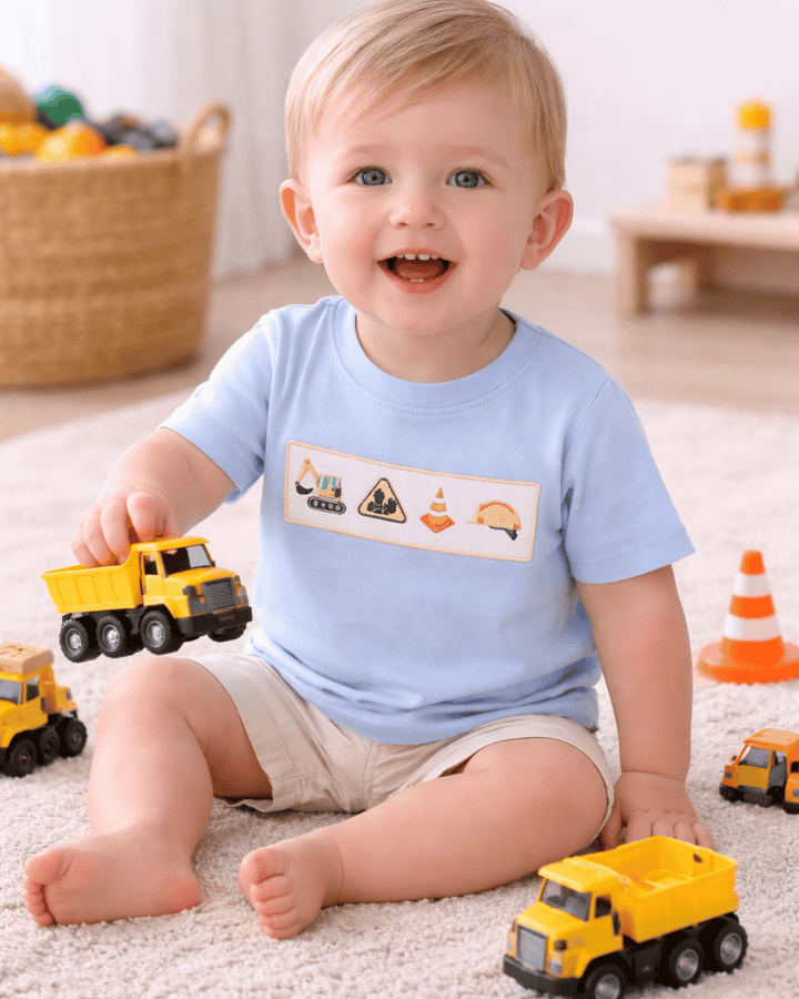 Child playing with toy trucks wearing a blue shirt with construction-themed graphics.