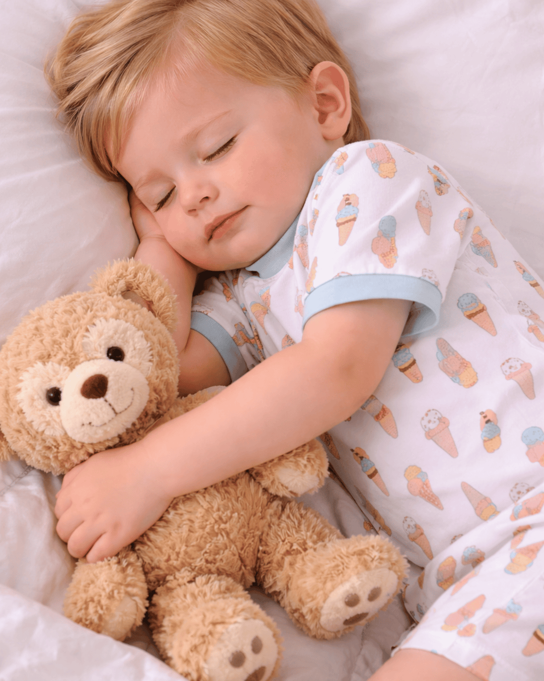 Child sleeping with a teddy bear, wearing pajamas with ice cream pattern