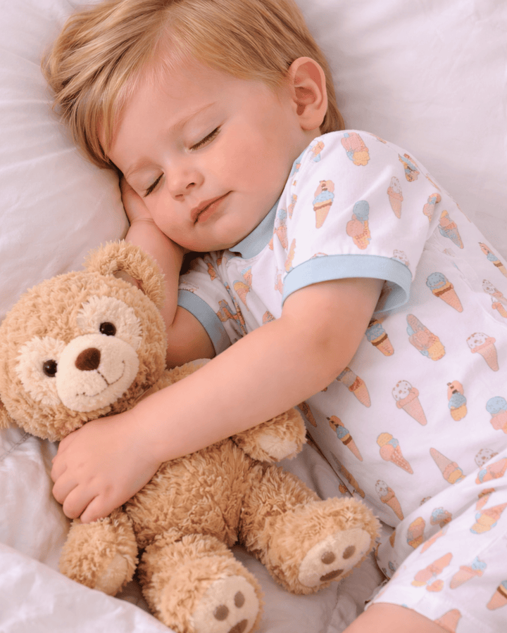 Child sleeping with a teddy bear, wearing pajamas with ice cream pattern