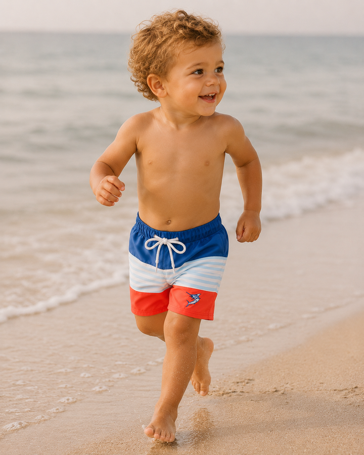 Child running on a beach wearing colorful swim shorts