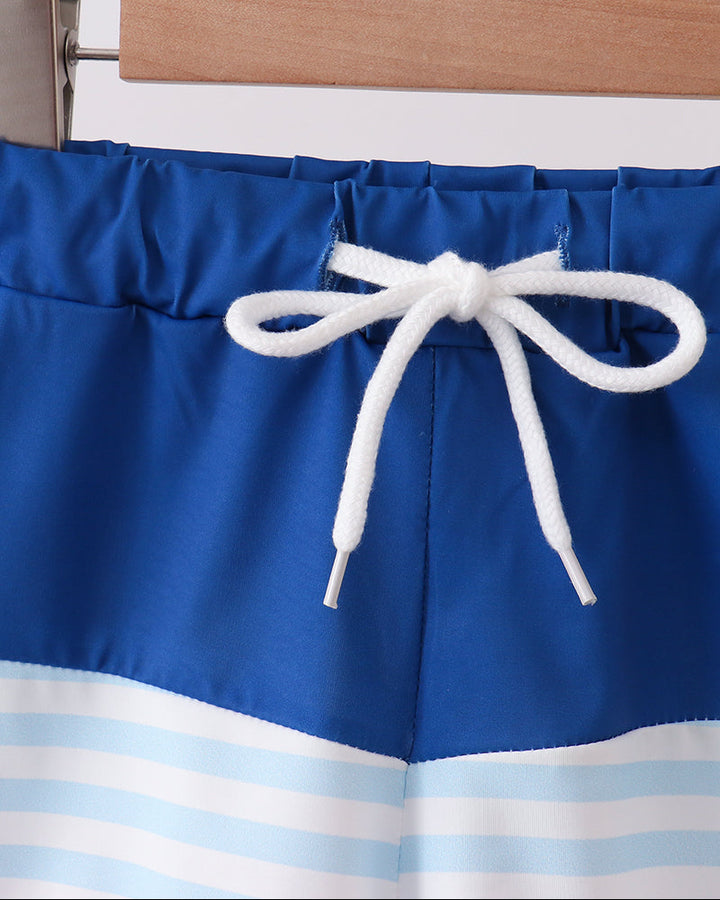 Blue swim shorts with white drawstring on a hanger against a white background