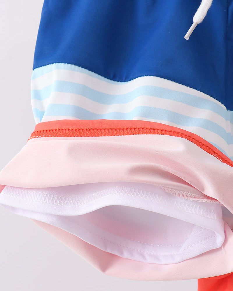 Close-up of a colorful swim trunks with blue, white, pink, and red stripes on a light gray background.