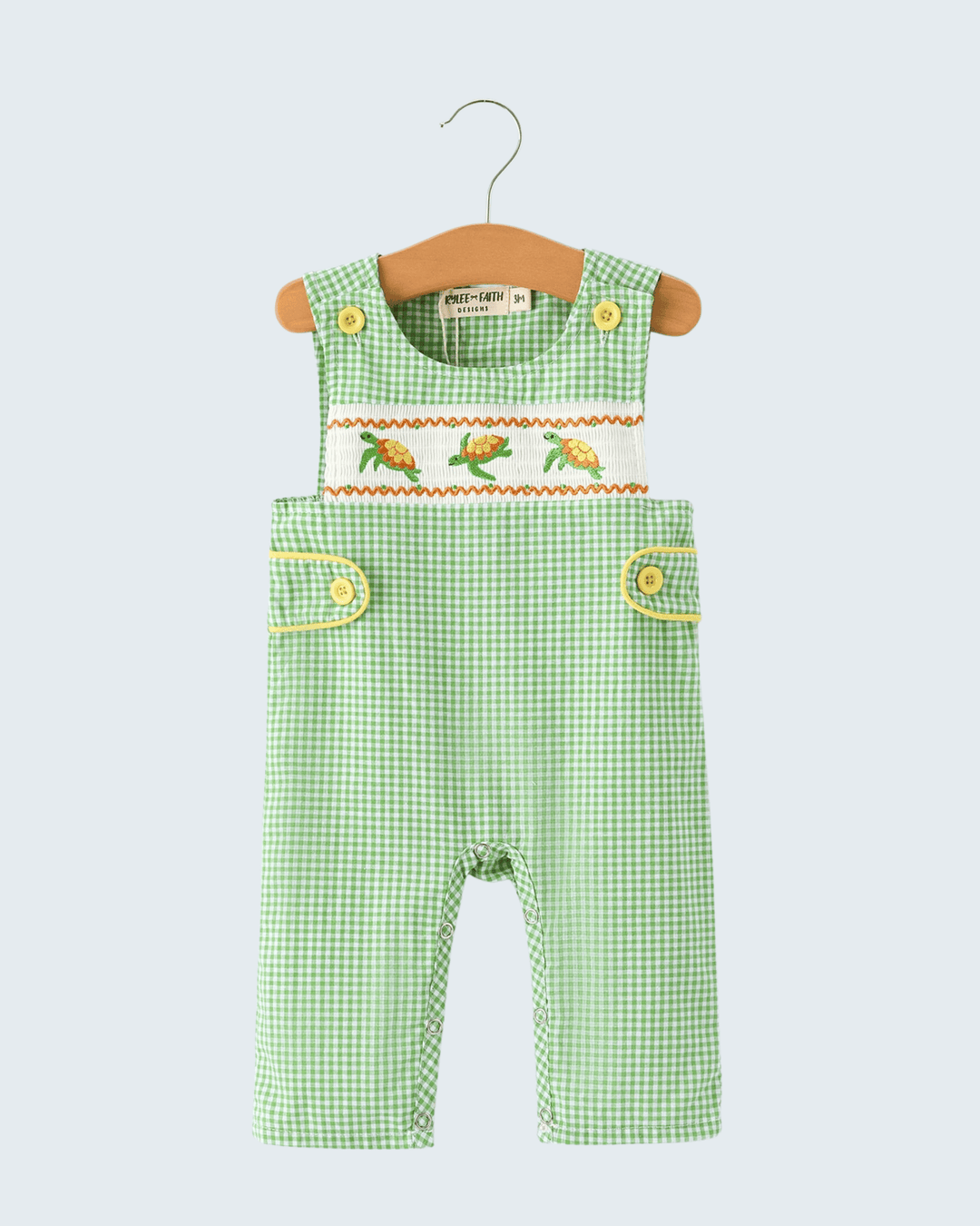 Green checkered overalls with embroidered details on a hanger against a light gray background
