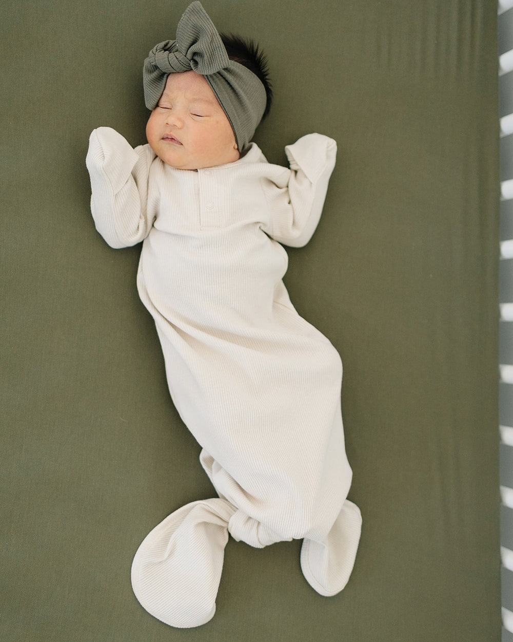 Newborn baby wrapped in a white swaddle with a gray headband on a green surface.