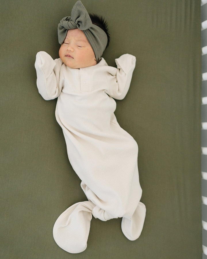 Newborn baby wrapped in a white swaddle with a gray headband on a green surface.