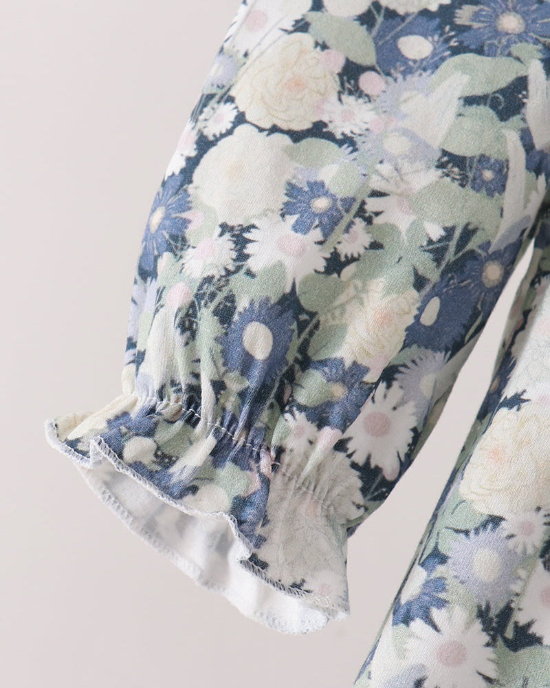 Close-up of a floral-patterned garment sleeve with a smocked elastic cuff, featuring blue, white, and pale green flowers on a light beige background.
