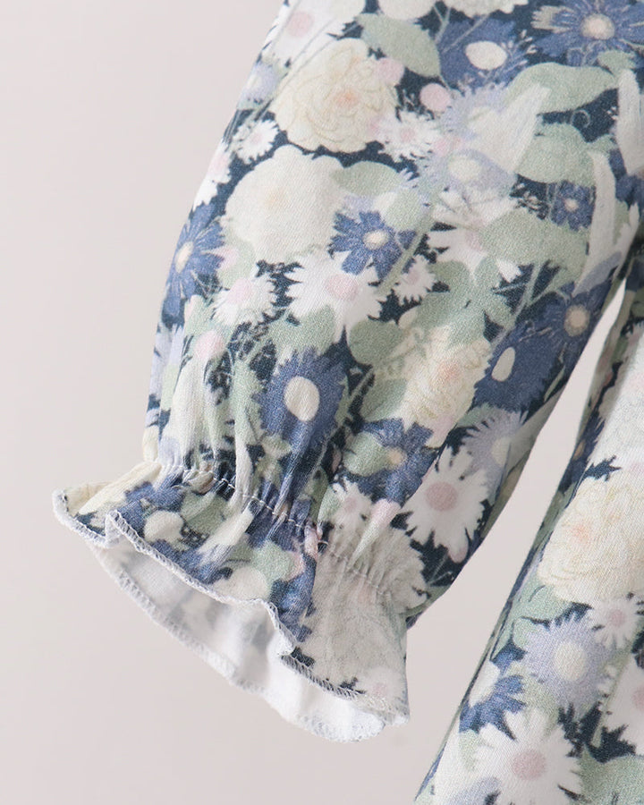Close-up of a floral-patterned garment sleeve with a smocked elastic cuff, featuring blue, white, and pale green flowers on a light beige background.