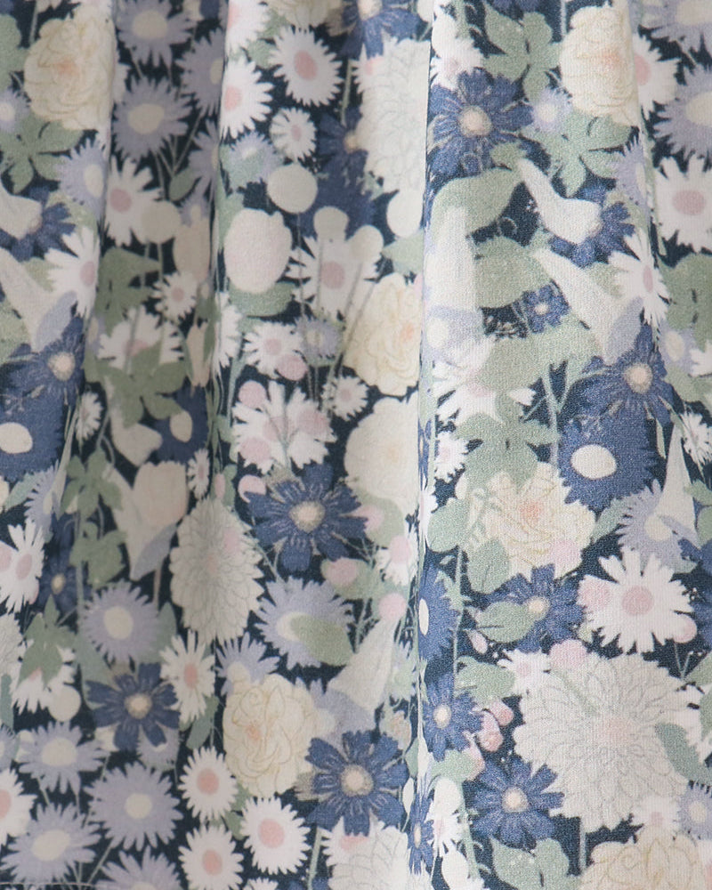 Close-up of a floral fabric with a repeating pattern of blue, white, and pale pink flowers with green leaves, shown in soft vertical folds.