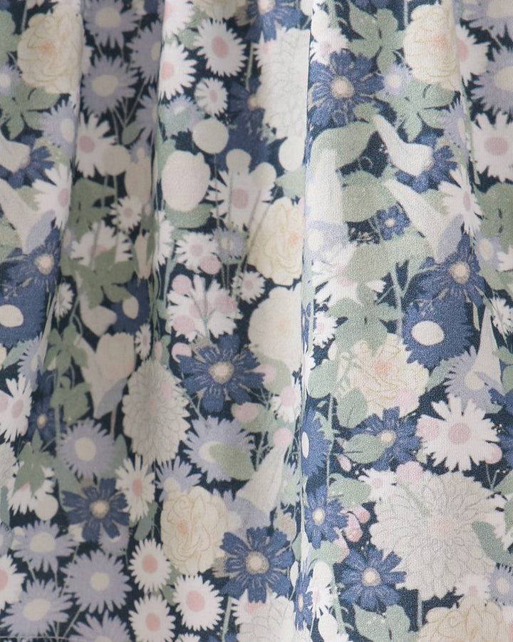Close-up of a floral fabric with a repeating pattern of blue, white, and pale pink flowers with green leaves, shown in soft vertical folds.