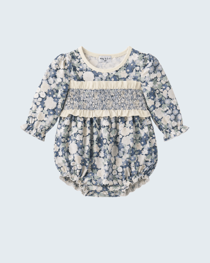 A baby long-sleeve romper in a blue and cream floral print, featuring a smocked chest panel and ruffle trim, shown flat on a light gray background.
