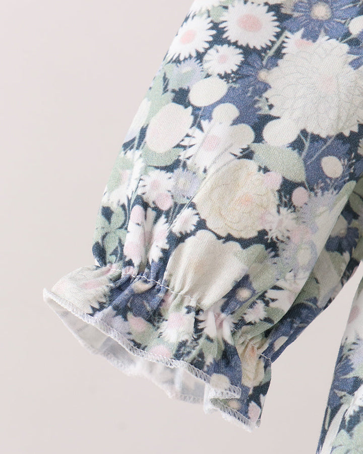 Close-up of a floral-patterned romper sleeve with a ruffled hem, featuring blue, white, and soft pink flowers on a light background.