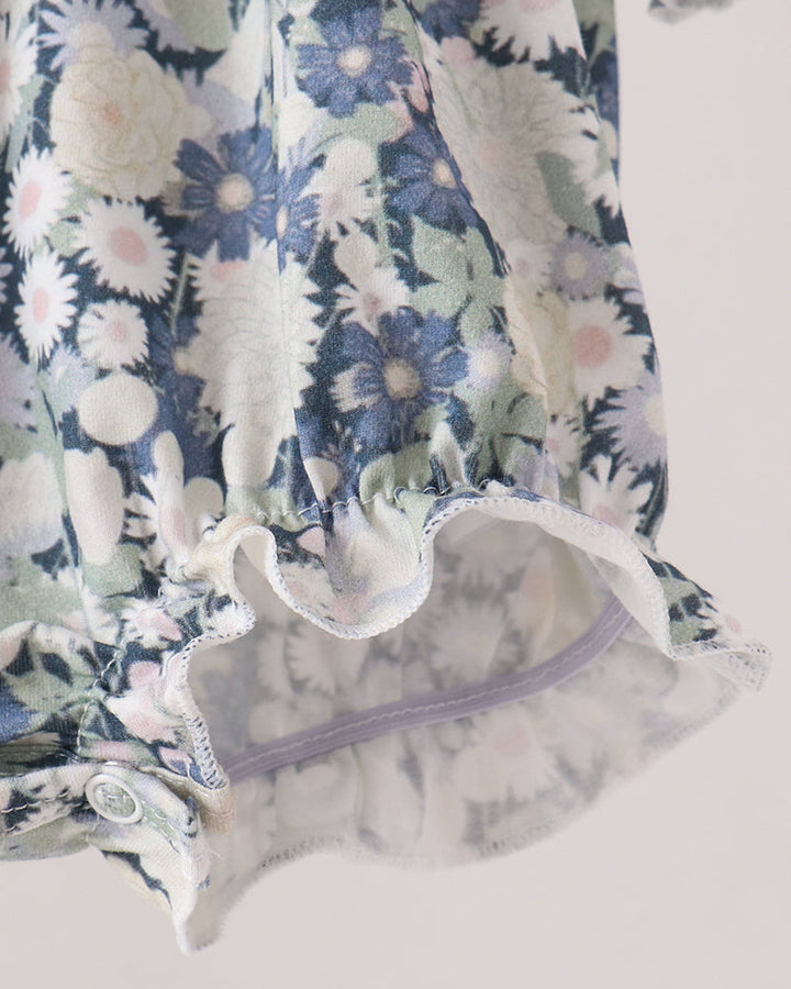 Close-up of a floral-patterned romper, featuring blue, white, and pale green flowers with a ruffled hem and a sheer inner lining.
