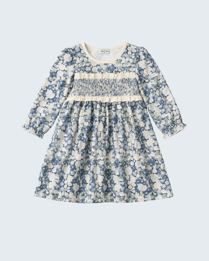 A long-sleeve dress with a blue and white floral print, featuring a smocked chest panel and cream trim, shown flat on a light gray background.