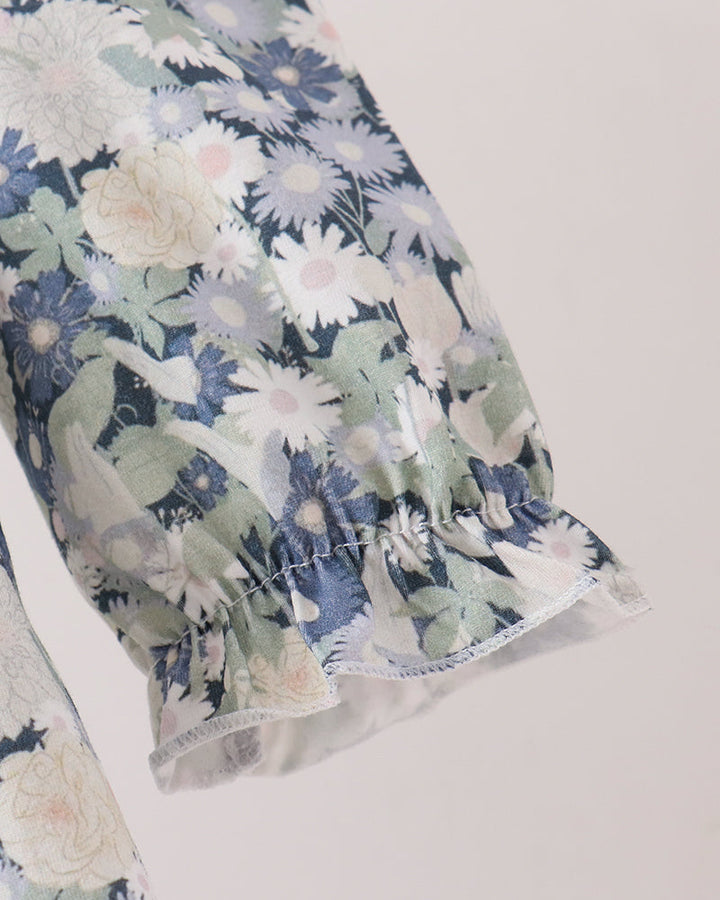 Close-up of a floral-patterned fabric sleeve with a ruffled hem, featuring white, blue, and green flowers on a light background.