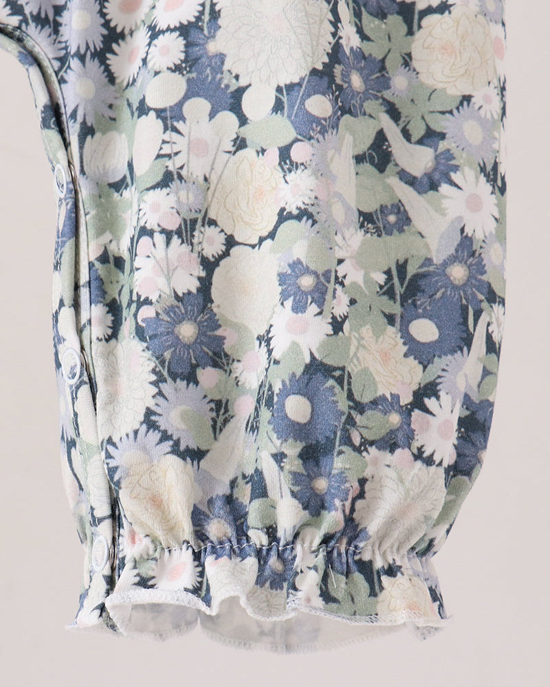 Close-up of a floral-patterned romper, featuring a blue, white, and pale green floral print with gathered elastic detailing at the bottom.