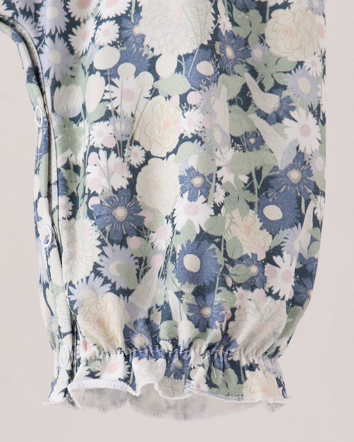 Close-up of a floral-patterned romper, featuring a blue, white, and pale green floral print with gathered elastic detailing at the bottom.