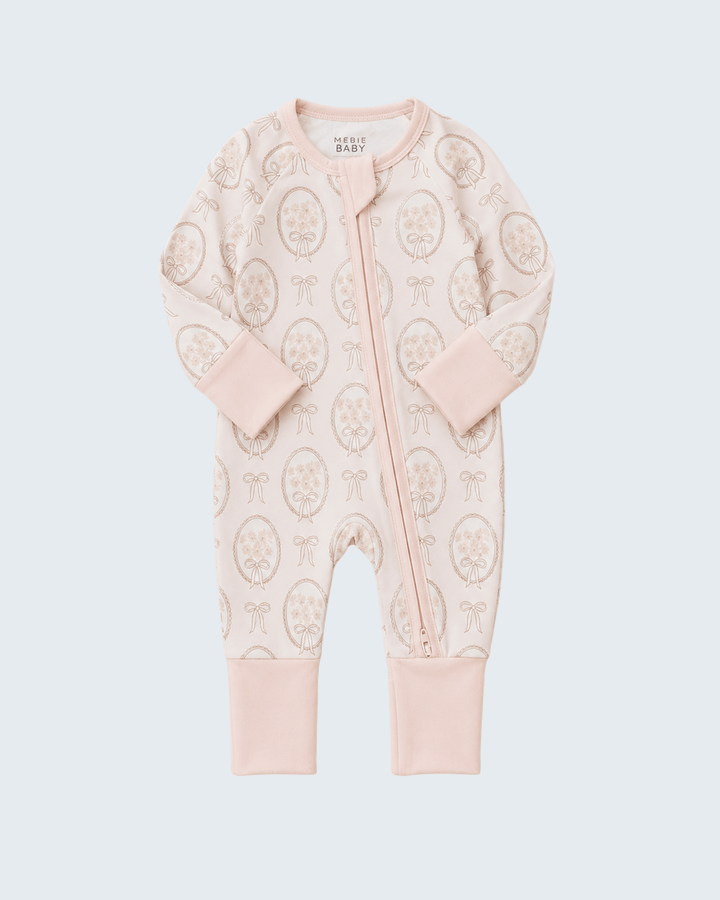 A baby long-sleeve footless one-piece sleeper in pale pink, featuring an all-over beige paisley pattern and a front zipper closure, shown on a light gray background.