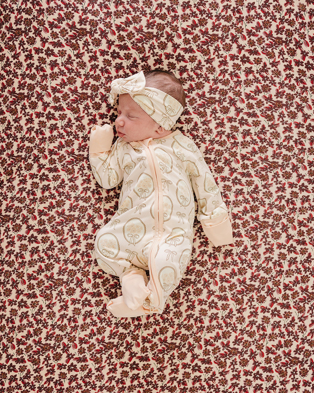 Cream patterned baby footed sleeper with front zipper, worn with matching hat