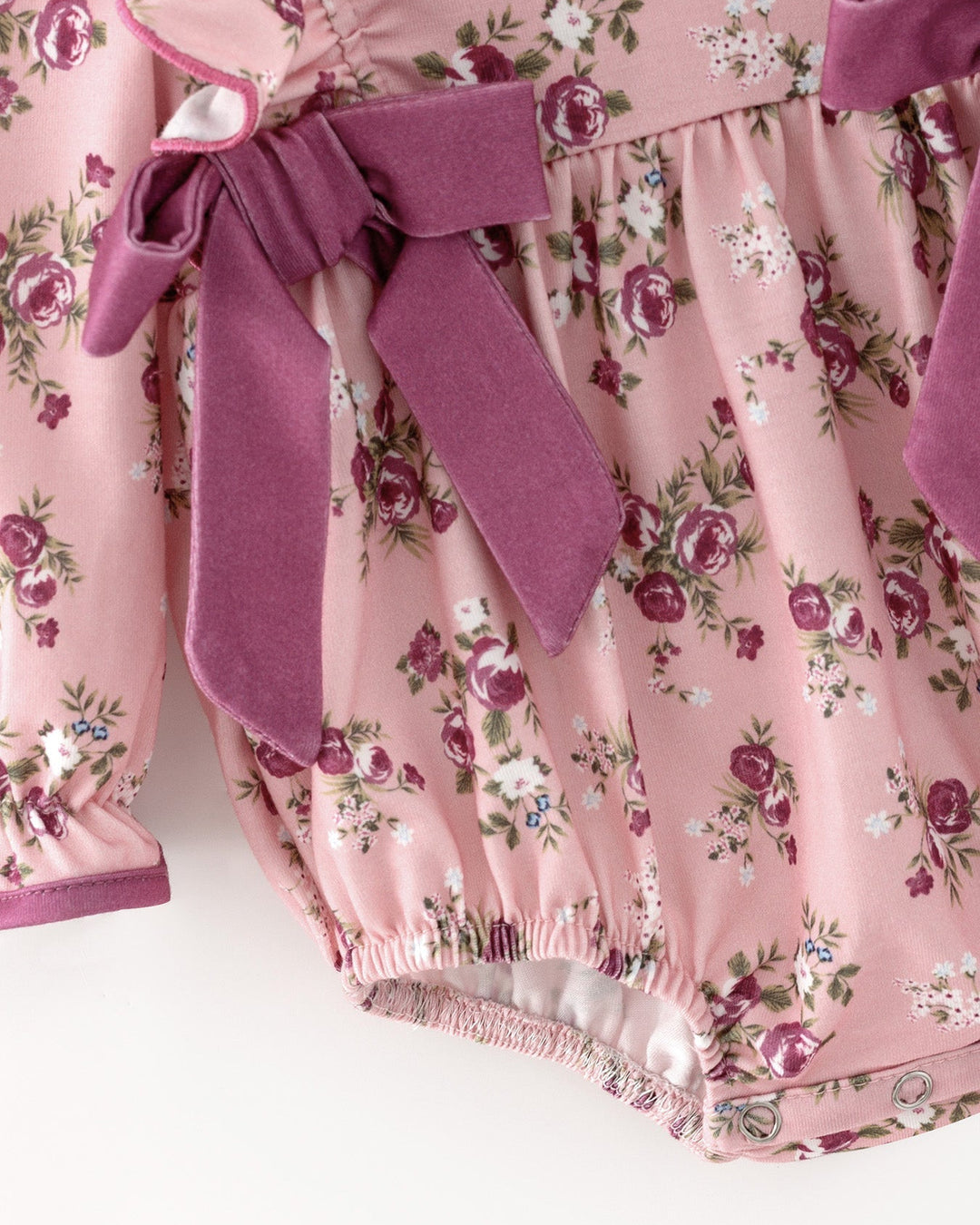 Pink floral romper with hanging purple bow ties and gathered leg hem