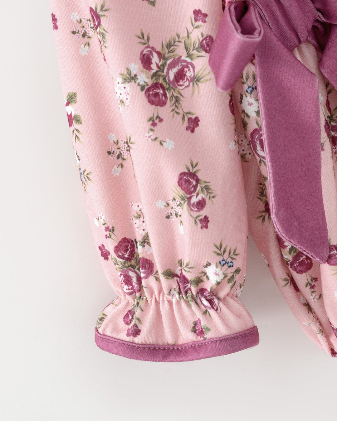 Pink floral baby romper with elastic cuffs and purple bow trim