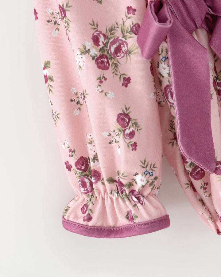 Pink floral baby romper with elastic cuffs and purple bow trim