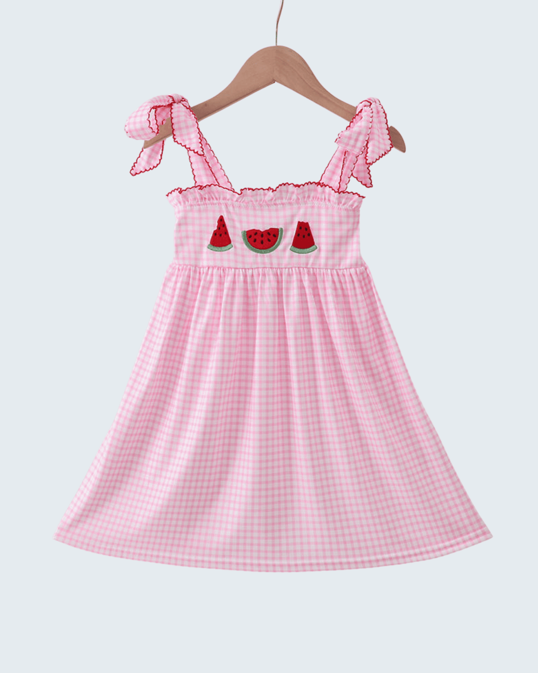 Pink checkered dress with watermelon design on a hanger against a white background